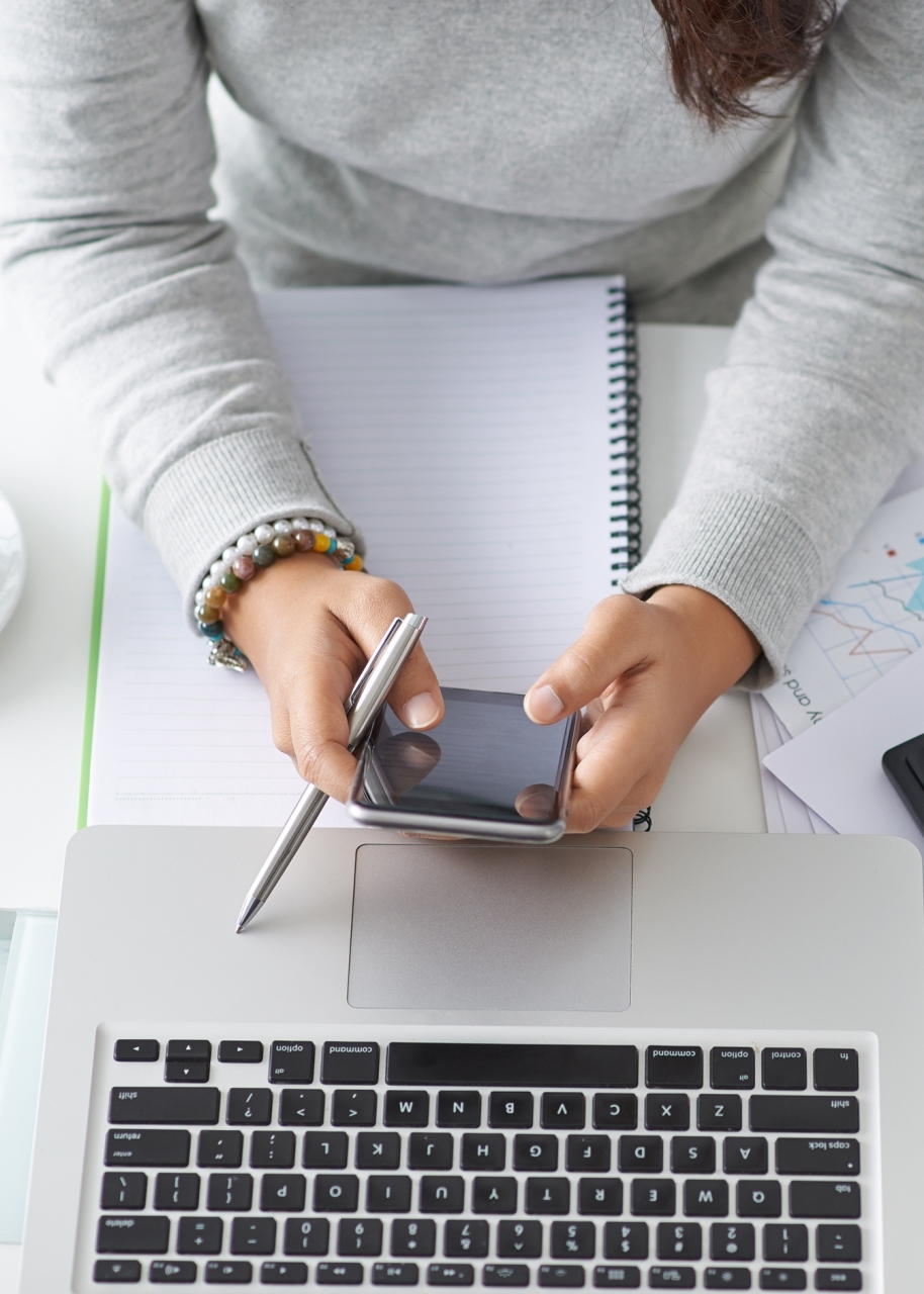 Woman at desk with phone, laptop, calculator, and financial documents